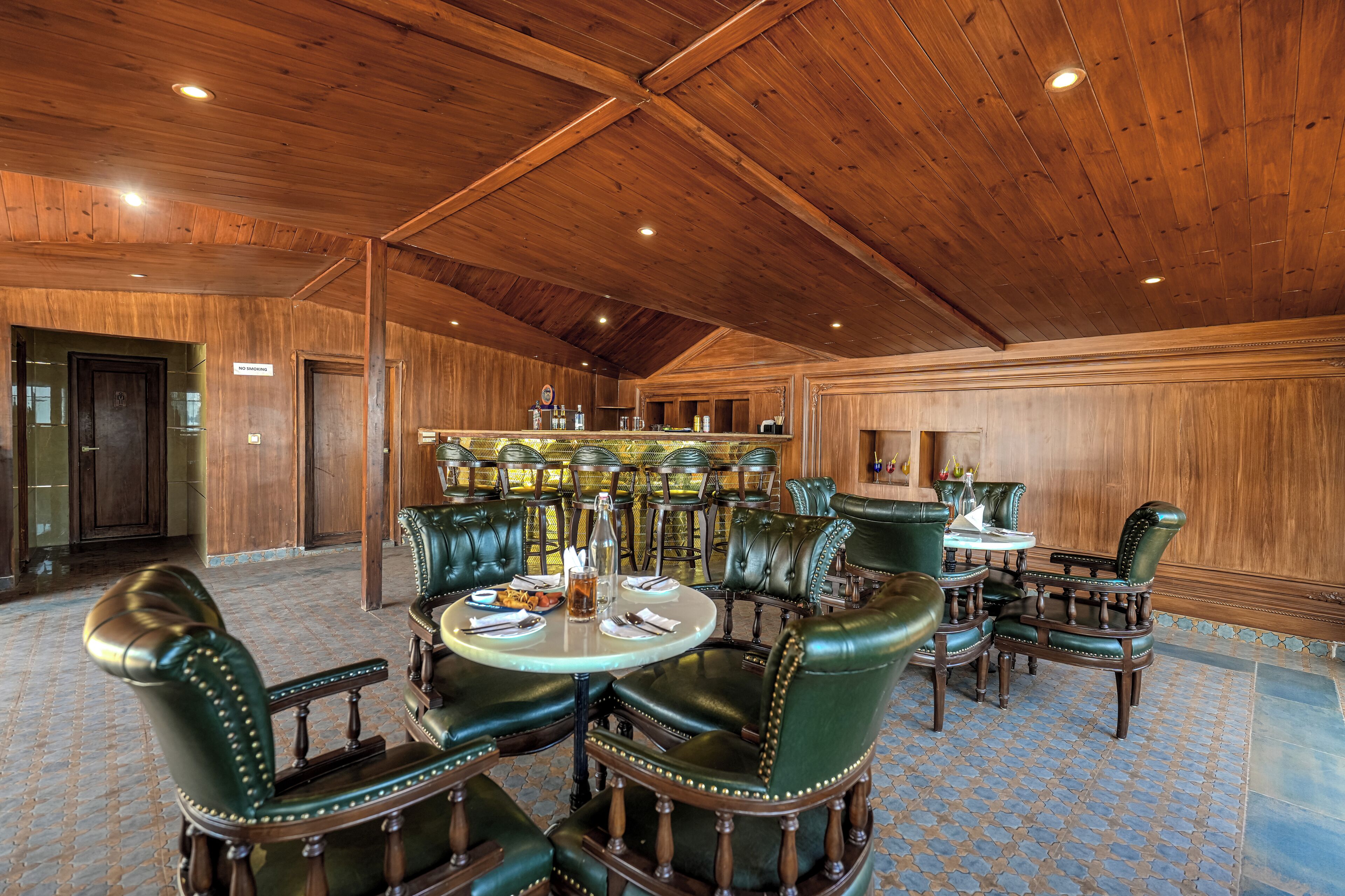 Une pièce spacieuse avec des plafonds et des murs en bois, des fauteuils en cuir, une table ronde et un coin bar.
