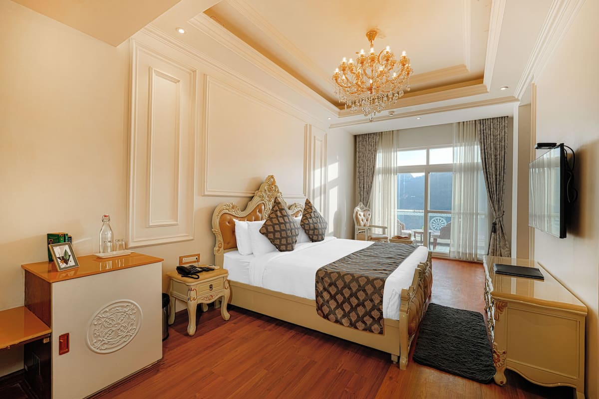 Ein Hotelzimmer mit einem großen Bett, einem Schreibtisch, einem Sessel, einem Fernseher und Blick ins Freie.