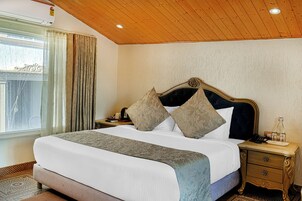 A neatly made bed with a headboard, a bedside table with a lamp, and a window with curtains.