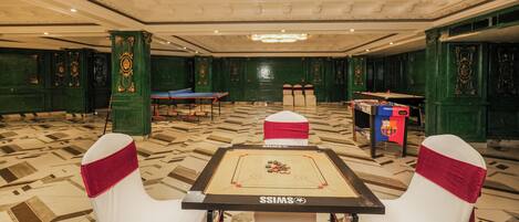 Una habitación amplia con mesa de fútbol de mesa, mesa de billar y sillas tapizadas de verde con fajas rojas.