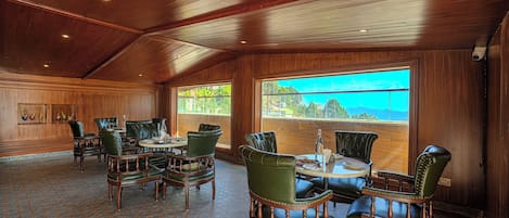 A dining area with wooden paneling, green upholstered chairs, and a large window offering a view of the outdoors.