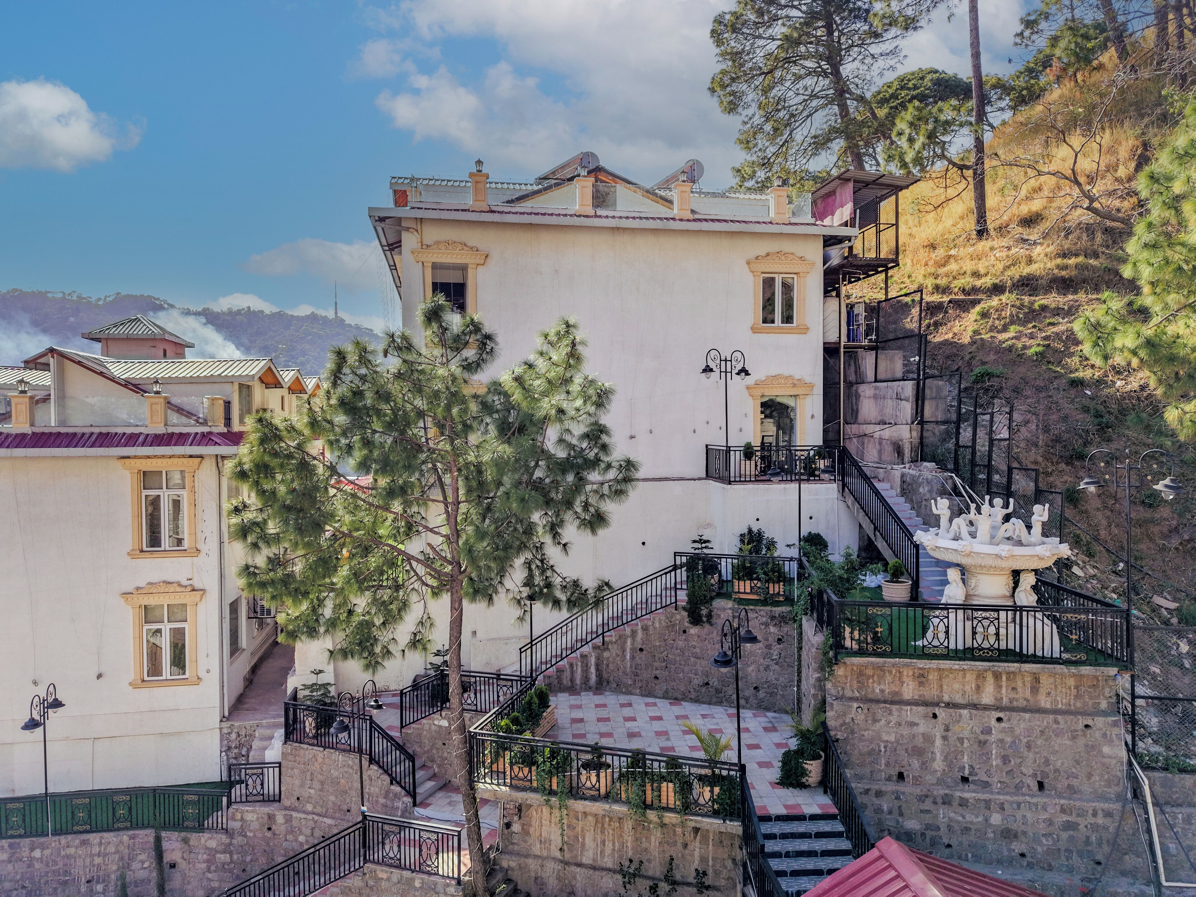 Ein mehrstöckiges Gebäude mit einer Treppe, die zu einem Balkon führt, umgeben von Bäumen und einer Berglandschaft.