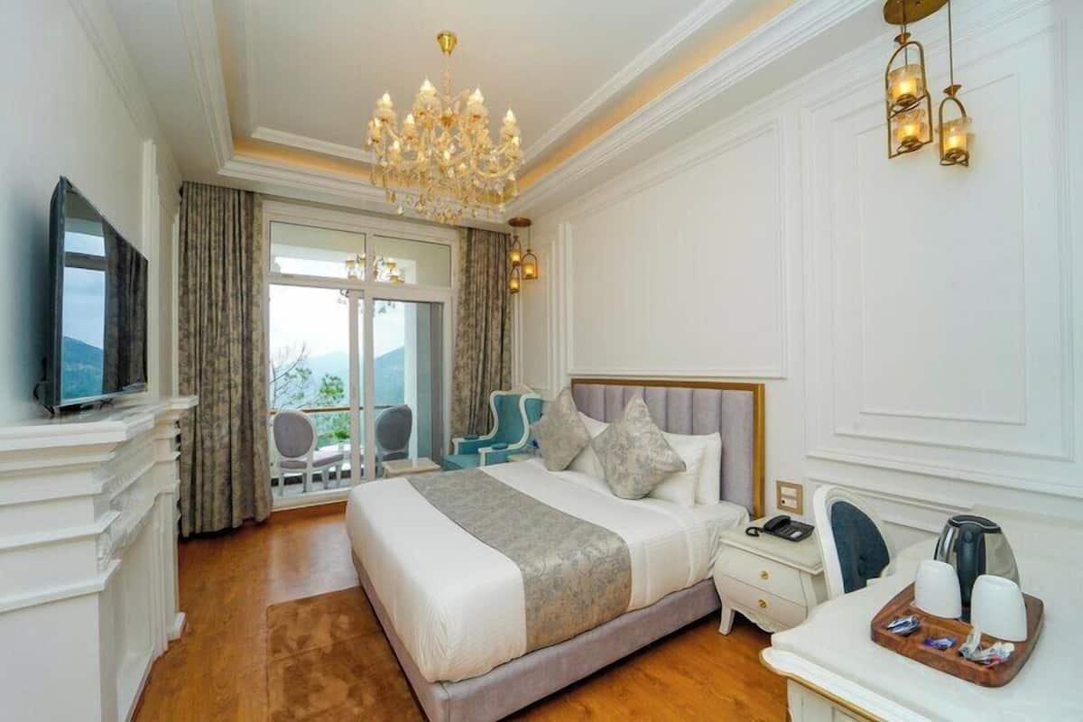 Ein Hotelzimmer mit einem großen Bett, einem Fernseher, einem Schreibtisch mit Kaffeemaschine und einem Balkon mit einem Stuhl.