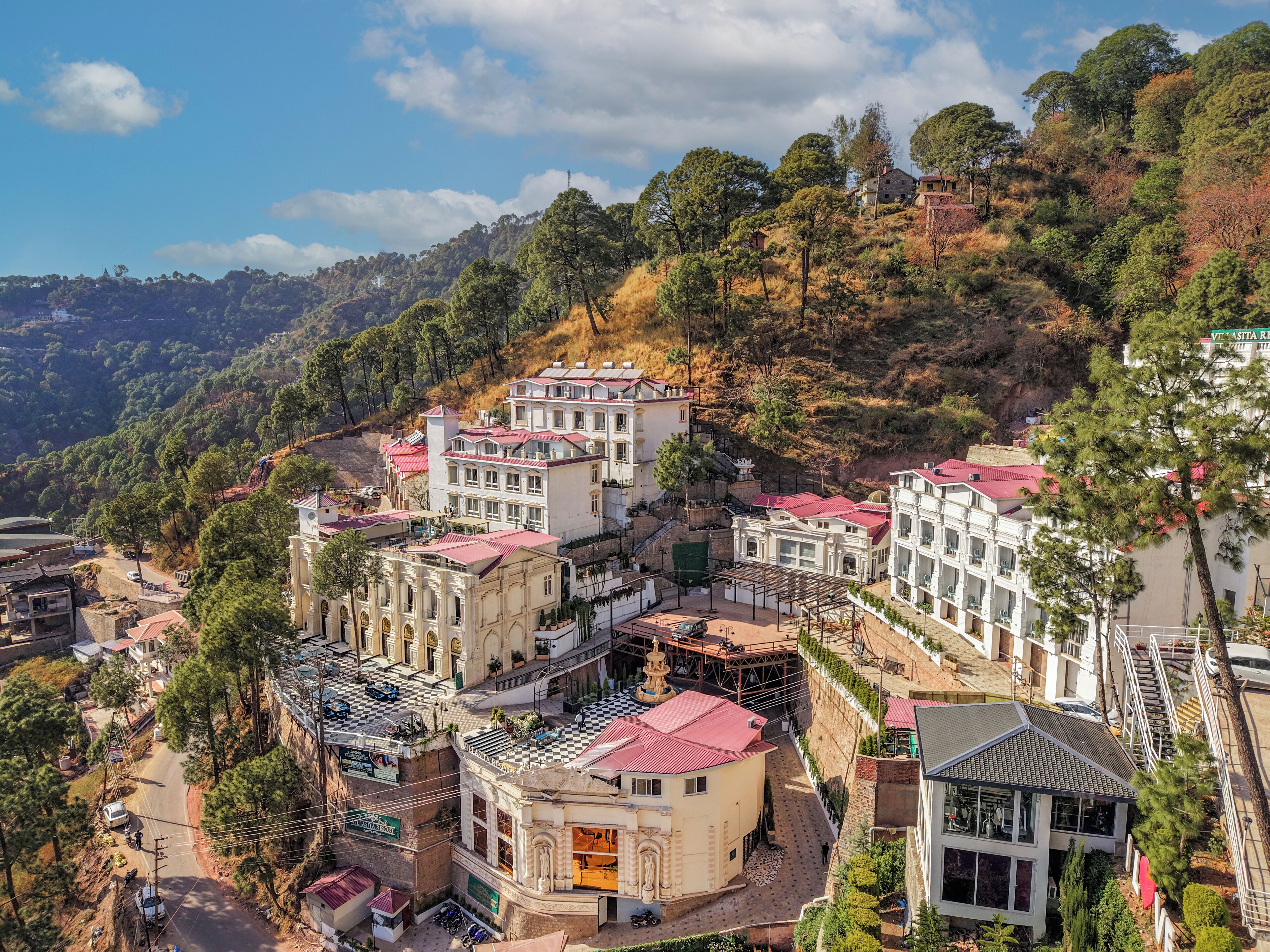 A hillside town with buildings featuring red-tiled roofs and white facades, surrounded by dense greenery and hills.