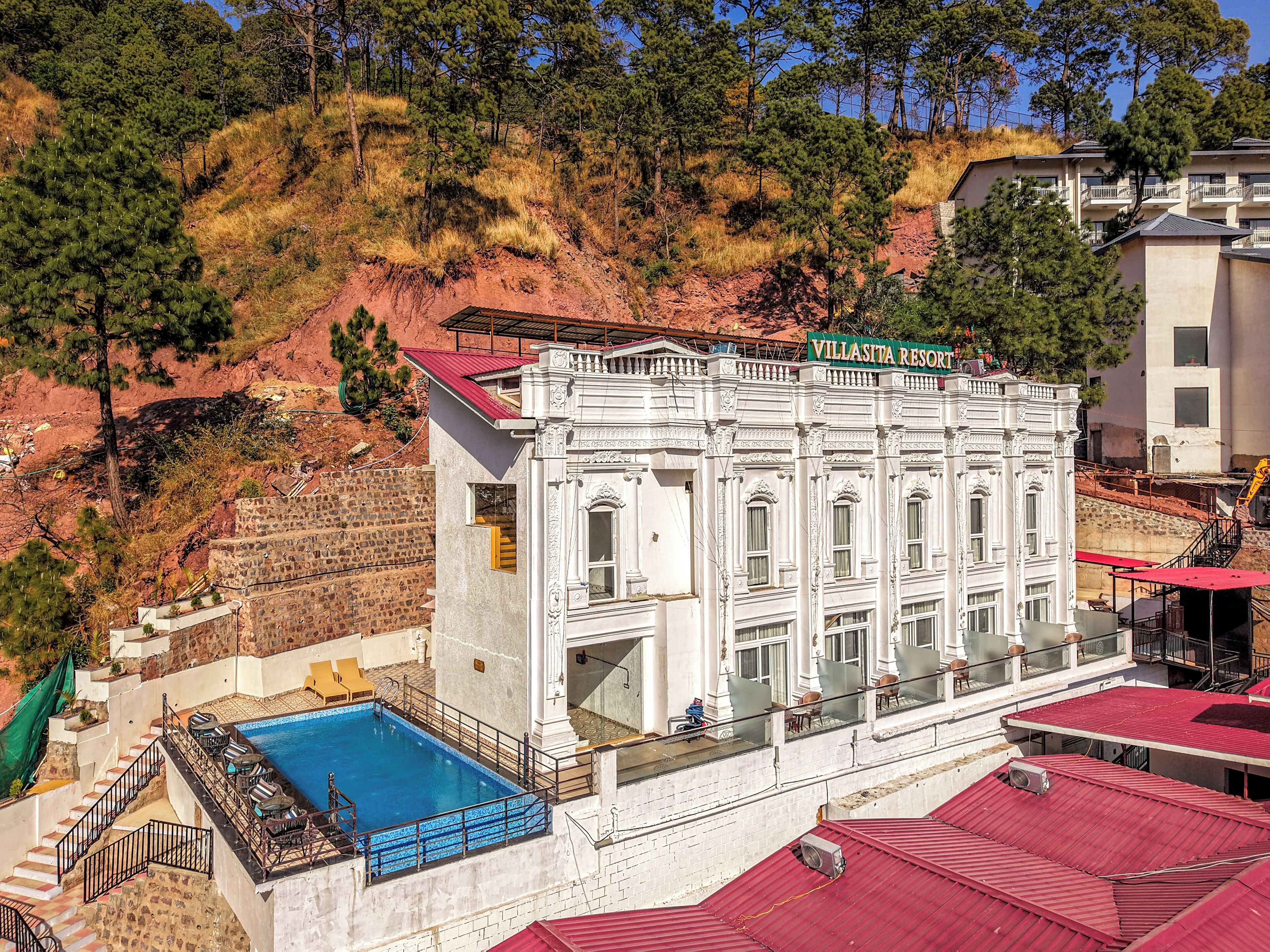 A white building with a sign reading "Villasita Resort" and a swimming pool with lounge chairs.