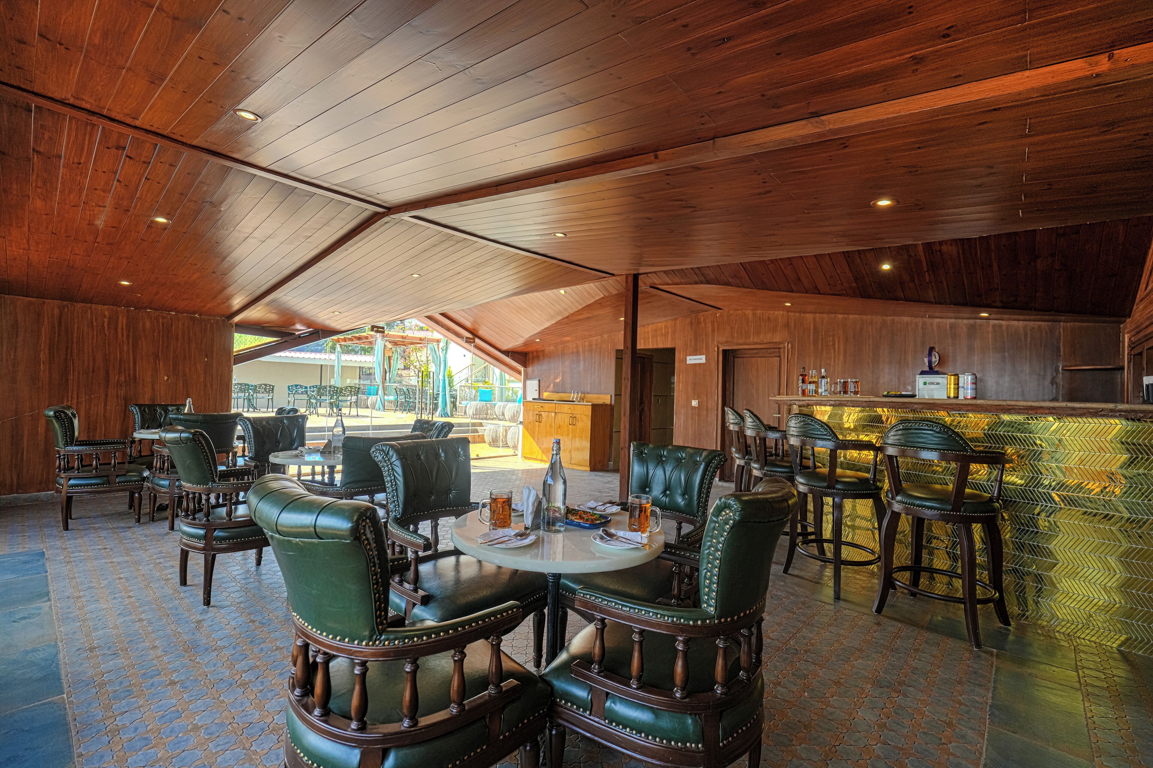 A spacious indoor area with wooden ceiling and walls, featuring a bar area with stools and a counter.