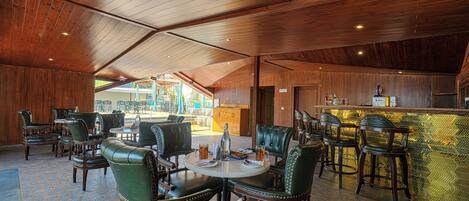 A spacious indoor area with wooden ceiling and walls, featuring a bar area with stools and a counter.