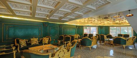 A room with ornate ceiling carvings, green upholstered furniture, and patterned flooring.