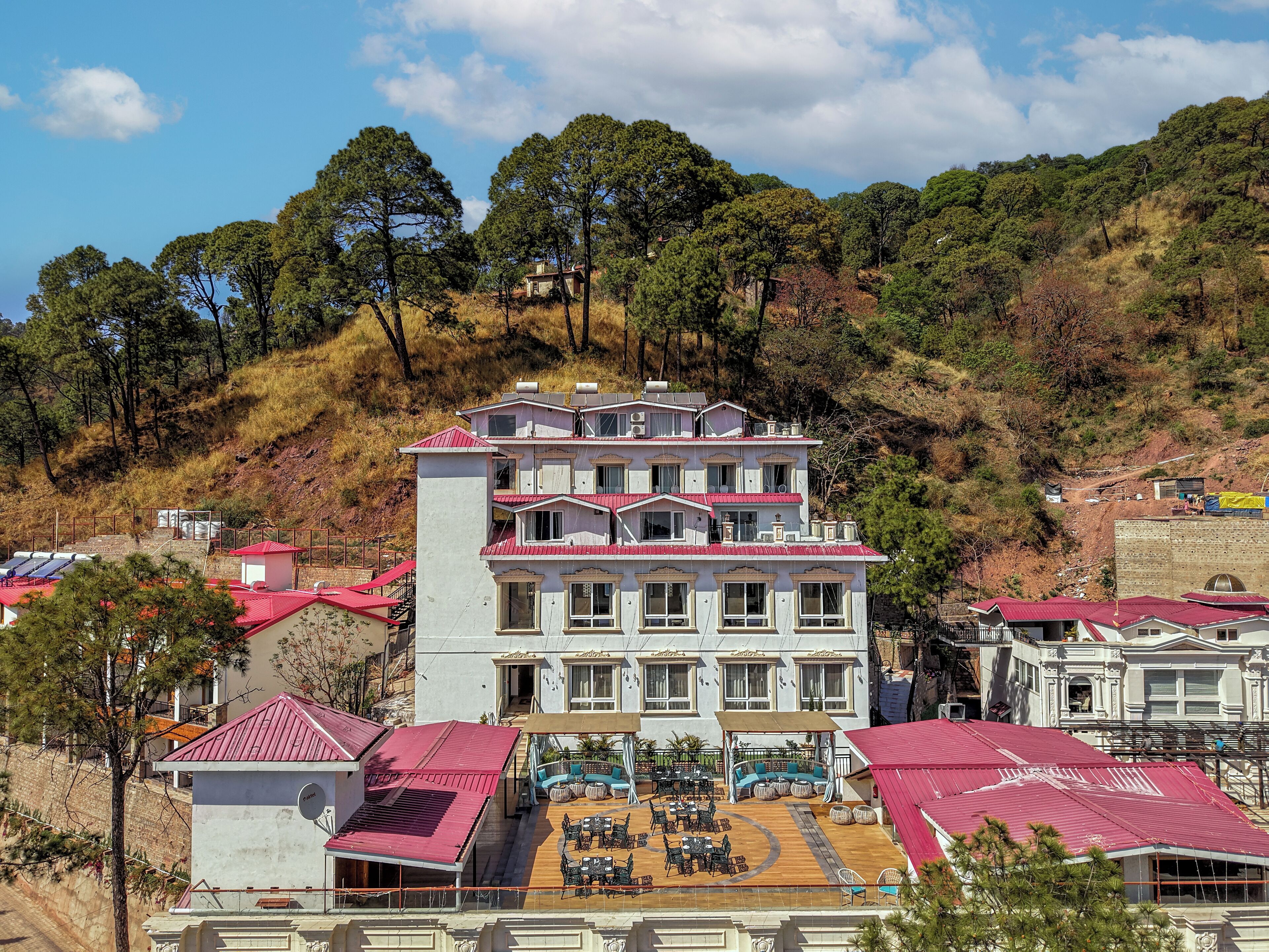 Un hotel de varios pisos con techo rojo, zona de estar al aire libre y vistas a un paisaje montañoso.