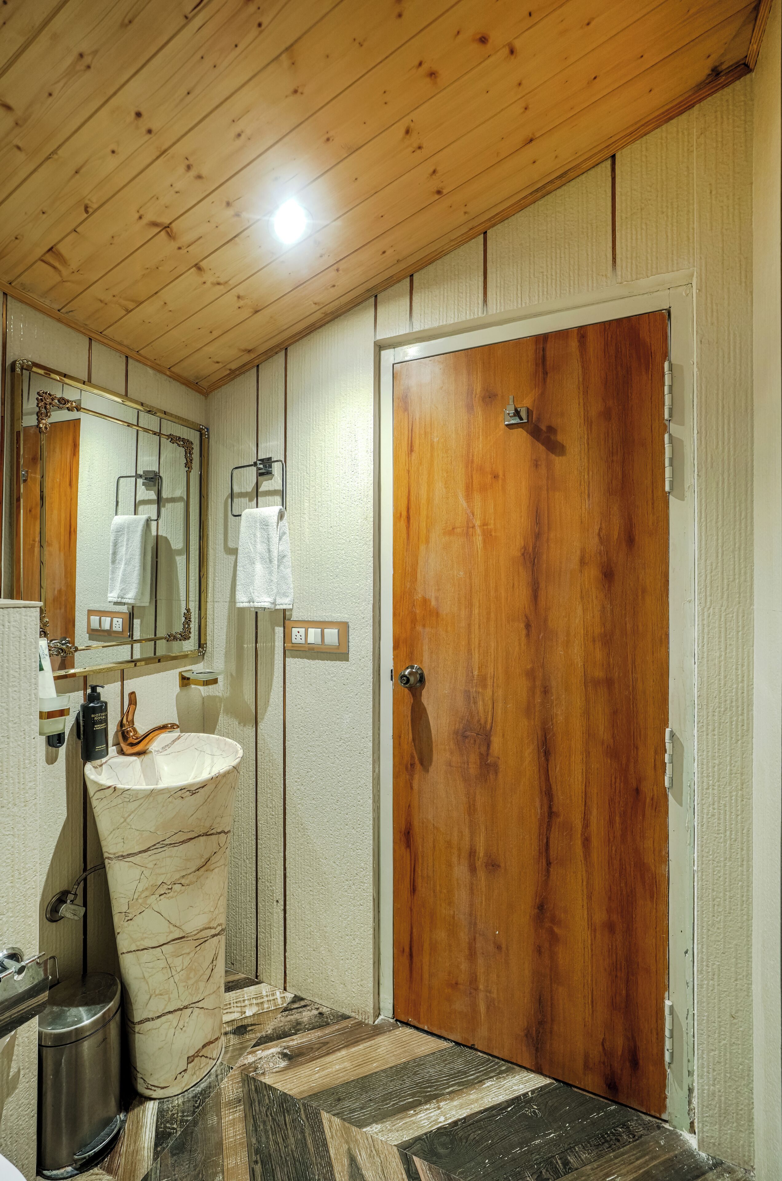 A bathroom with a wooden ceiling, a marble sink, a wooden door, and a mirror with a towel hanging on it.