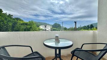 A balcony with two chairs and a small table, overlooking a residential area with houses and greenery under a cloudy sky.