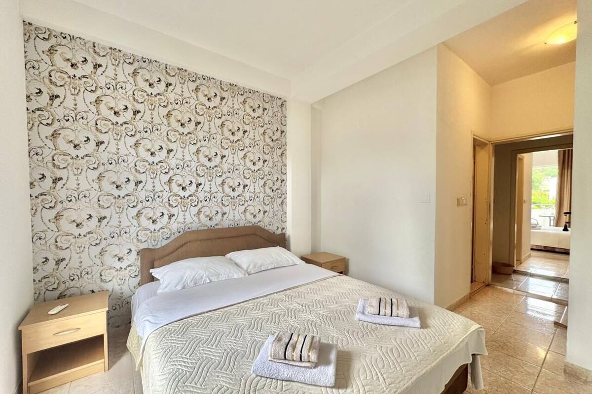 Een net opgemaakt bed met een hoofdbord met patroon, een nachtkastje en een muur met bloemenbehang.