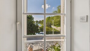 A window with a view of a green park, a pathway, and a parked car. - Sea view, 50 m from the port, House for 6, Garden (Le Croisic)