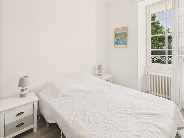 A bedroom with a single bed, two bedside tables, and a window with a view of greenery.