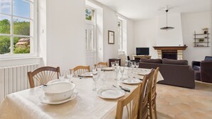 A dining area with a table set for six, a fireplace, a television, and a sofa in a bright room with large windows. - Sea view, 50 m from the port, House for 6, Garden (Le Croisic)