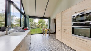 A modern kitchen with a large window, built-in oven, and a dining area with a table and chairs.