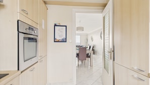A modern kitchen with stainless steel appliances, a dining area with a table and chairs, and a view into the living room.