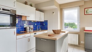Eine moderne Küche mit weißen Schränken, einem eingebauten Backofen, einer Kaffeemaschine und einem Fenster mit Blick auf Grünflächen.