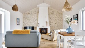 A living room with a stone wall, a fireplace, a sofa, and a dining table with chairs. - Heated pool, garden, villa for 8 adults 2 children (La Guérinière)