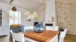A dining area with a wooden table, white chairs, and a blue vase with dried plants. - Heated pool, garden, villa for 8 adults 2 children (La Guérinière)