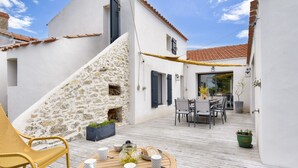 A patio with a round table, chairs, and a stone wall. - Heated pool, garden, villa for 8 adults 2 children (La Guérinière)