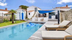 A swimming pool with lounge chairs, a blue inflatable shark, and a stone wall. - Heated pool, garden, villa for 8 adults 2 children (La Guérinière)