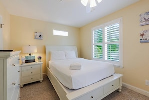 Une chambre à coucher comprenant un lit, une table de chevet, une commode et une fenêtre avec des stores.