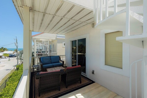 A balcony with wicker furniture, a sliding glass door, and a view of the street and ocean. - Relaxing 3 Bdr Keys Retreat - Hate to leave it (Marathon)