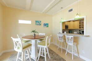 A dining area with a round table and four chairs, a kitchen with a countertop and cabinets, and a hanging light fixture.