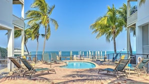 A pool area with lounge chairs, palm trees, and a view of the ocean.