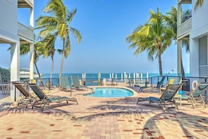A pool area with lounge chairs, palm trees, and a view of the ocean.
