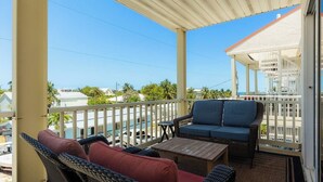 A covered balcony with wicker furniture, a small table, and a view of the ocean and buildings.