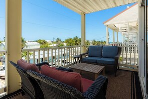 A covered balcony with wicker furniture, a small table, and a view of the ocean and buildings.