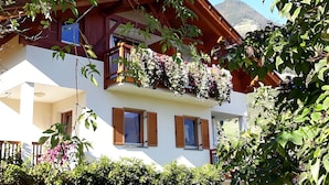 A two-story building with wooden balconies, white walls, and a mountain backdrop. - Apartment 'Sonnenblume' with Mountain View, Wi-Fi and Air Conditioning (Lagundo)