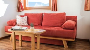 A red sofa with a small table in front, a window with curtains, and a plant on the table. - Apartment 'Sonnenblume' with Mountain View, Wi-Fi and Air Conditioning (Lagundo)