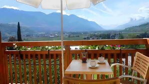 A wooden deck with a table and chairs, an umbrella, and a scenic mountain view. - Apartment 'Mohnblume' with Mountain View, Wi-Fi and Air Conditioning (Lagundo)