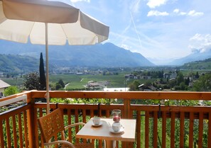 A balcony with a table, chairs, and an umbrella, overlooking a scenic valley with mountains.
