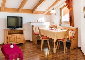 A cozy room with a wooden dining table, chairs, a television, and a small table with a vase.