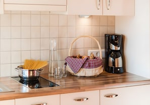 A kitchen with a pot of spaghetti, a glass, a basket with bread, and a coffee maker.
