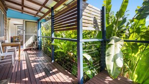 Una terraza de madera con barandilla metálica, rodeada de abundante follaje verde.
