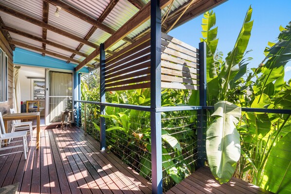 A wooden deck with a metal railing, surrounded by lush green foliage.