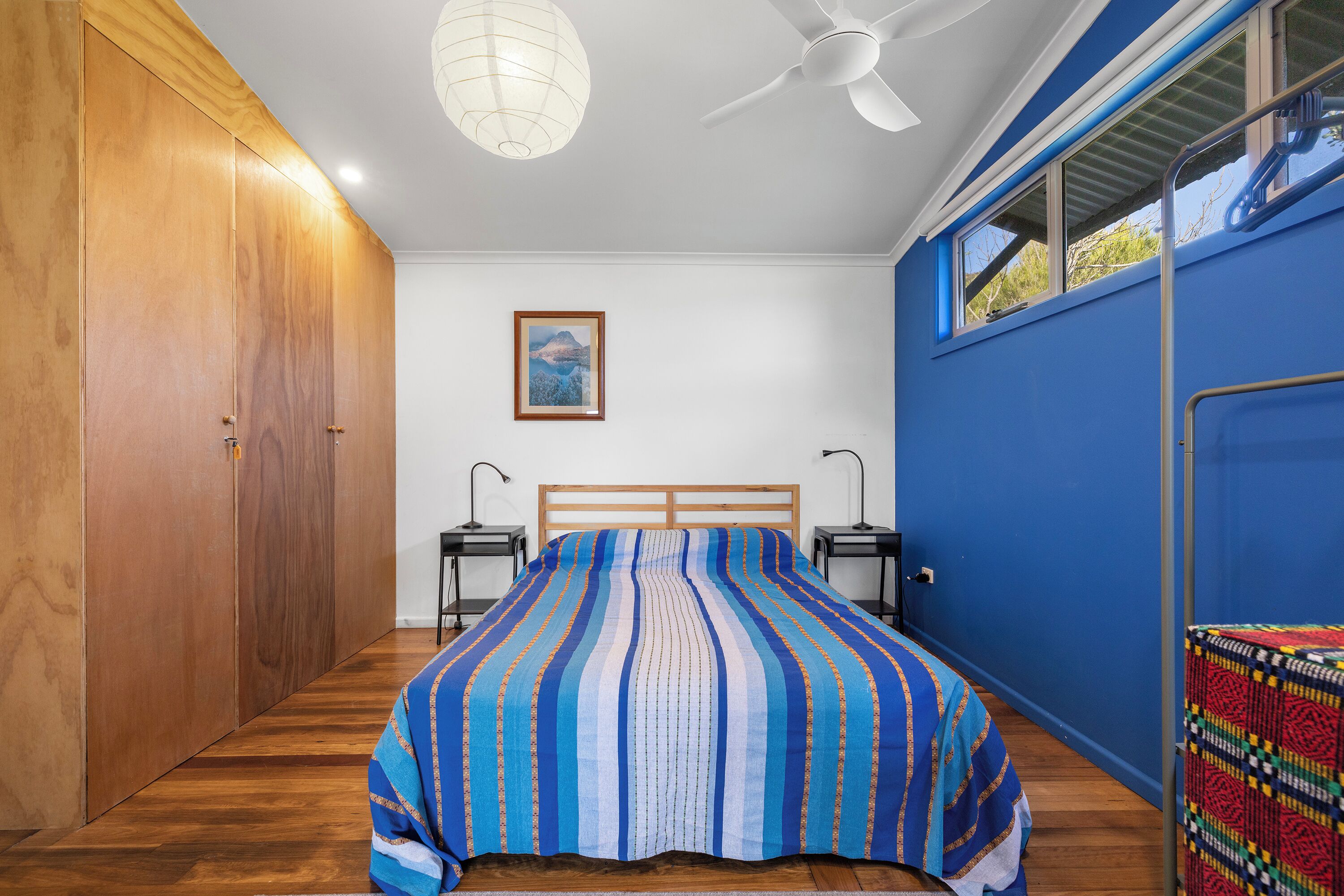 A bedroom with a large bed, wooden wardrobe, ceiling fan, bedside lamps, and a window with a view.