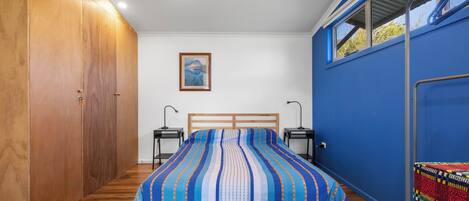 A bedroom with a large bed, wooden wardrobe, ceiling fan, bedside lamps, and a window with a view.