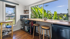 Una cocina con un ventanal grande, taburetes de madera, un lavamanos y un refrigerador pequeño.