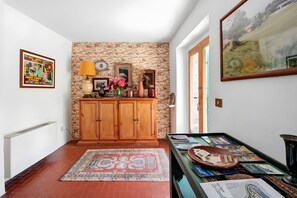 A hallway with a patterned wallpaper, a wooden cabinet, a lamp, and a rug.