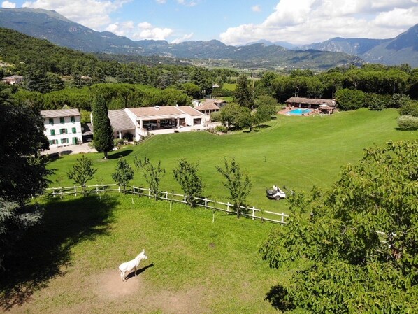 A rural landscape with a large grassy field, a white building with multiple windows, and a mountain range in the background.