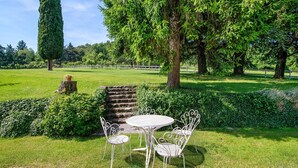Ein Garten mit einem weißen Metalltisch und -stühlen, umgeben von üppigem Grün und Bäumen.