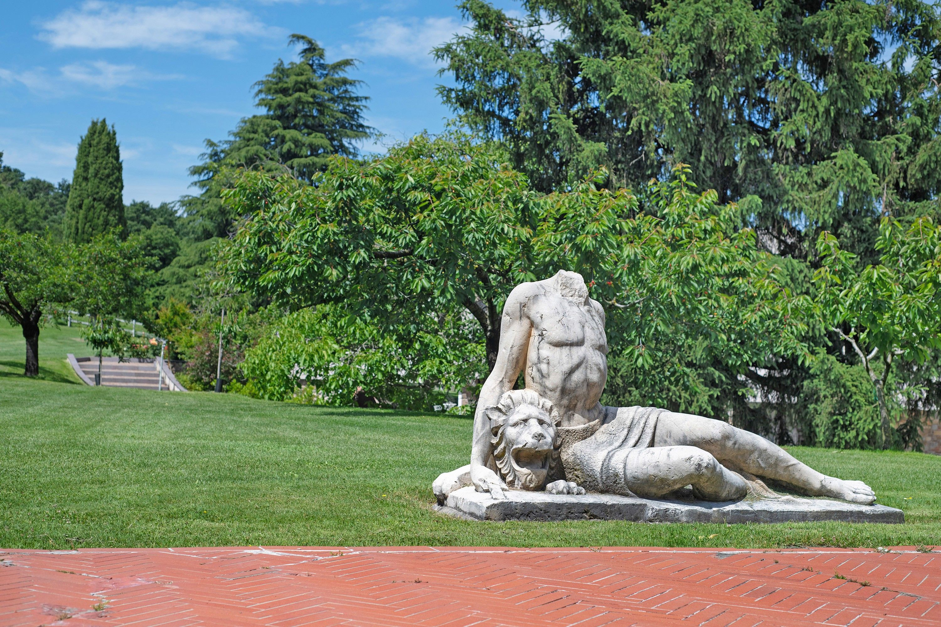 Estátua de uma figura reclinada com um leão em um parque.