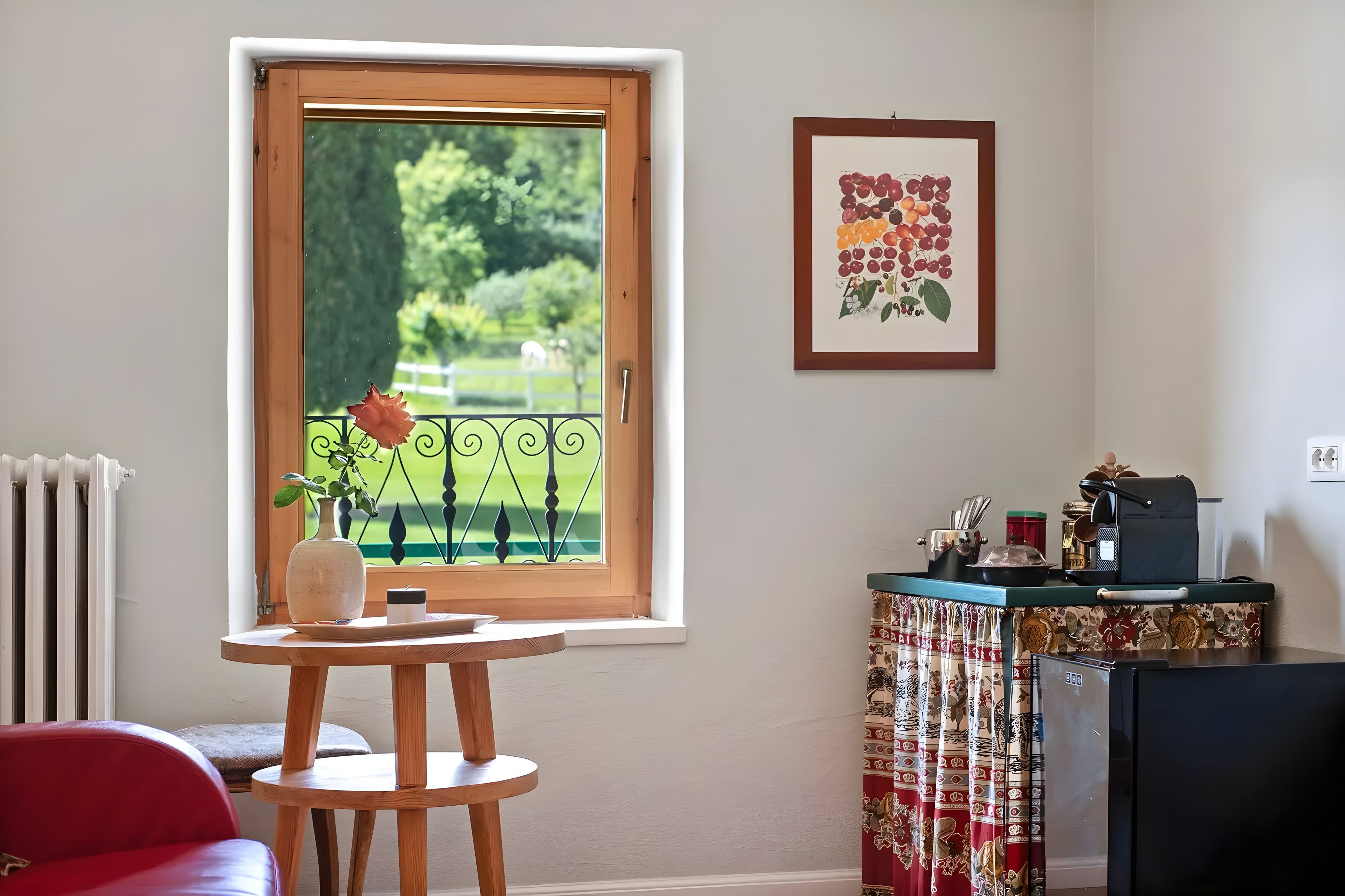 Ein Zimmer mit Fenster, Tisch mit Vase, Stuhl, Heizkörper und Wand mit einem gerahmten Bild.