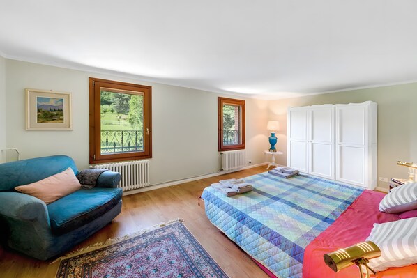 A bedroom with a bed, a sofa, a radiator, a window, and a wardrobe.